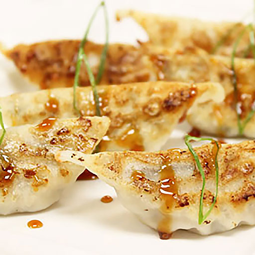 Chicken Gyoza dumplings with a glossy sauce and green onions on a white background