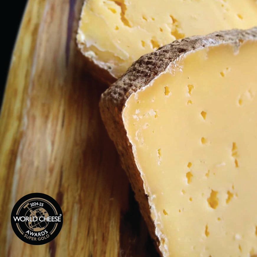 Close-up of a wedge of semi-hard Nightshade cheese with a dark rind and characteristic holes, resting on a wooden cutting board. A circular 'World Cheese Awards Super Golds' badge is visible in the bottom-left corner.