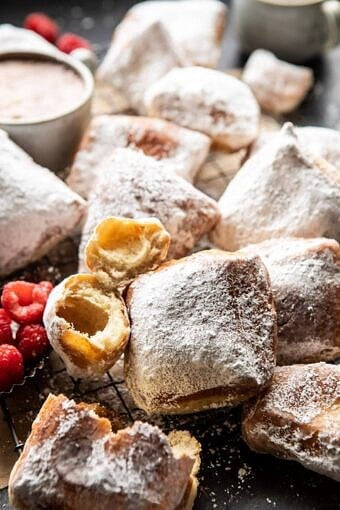 Powdered-sugar beignets on a wire rack with raspberries and a bowl of sauce