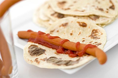 Hot dog on a tortilla with ketchup on a white plate