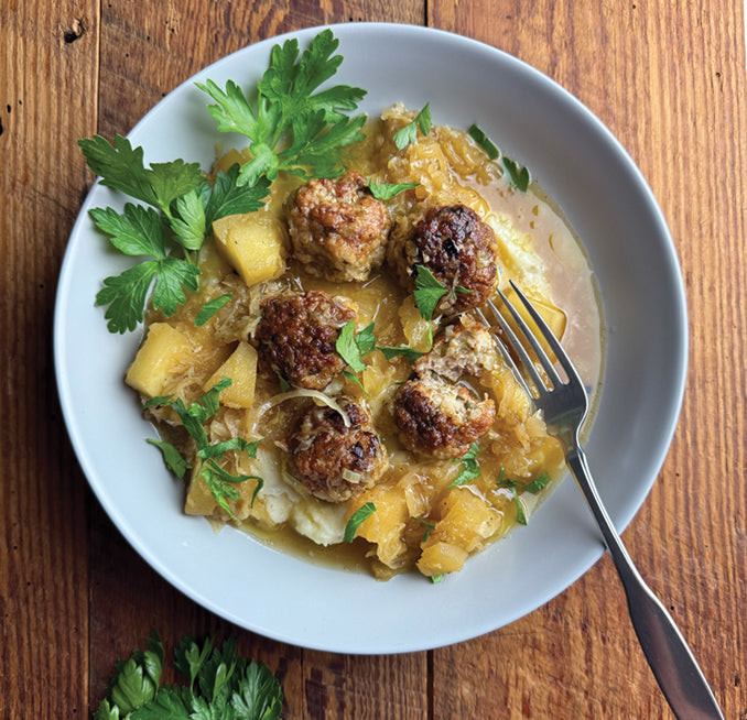 Browned meatballs with potato pieces, sauce and parsley on a white plate