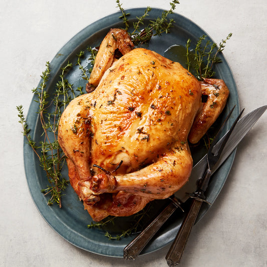 Roasted chicken on a blue plate with herbs and utensils on a light gray background