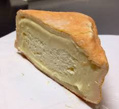 A triangular slice of Foxglove cheese  with a golden-brown crust and a thick pale yellow creamy filling, shown on a white plate or surface.