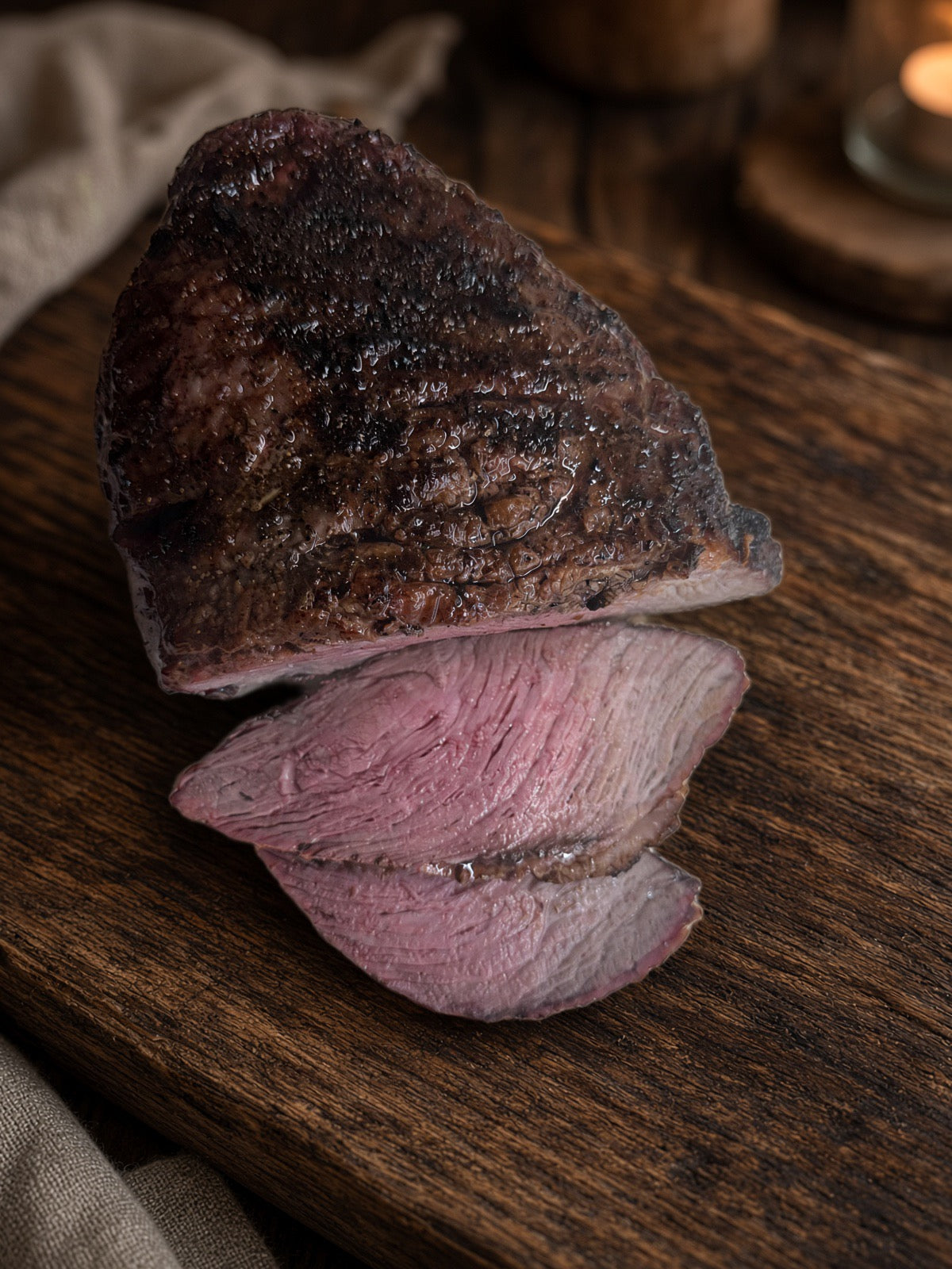  close-up roast on a dark board, received the other photo’s text. Replace it with: Browned culotte beef roast with two slices showing the pink center on a wooden cutting board