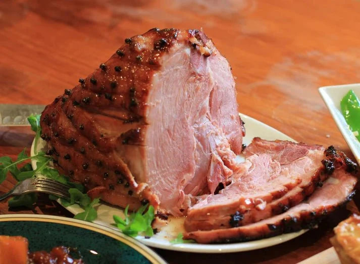 A close-up of a sliced ham or roast on a white plate, with a fork and garnish on a wooden table.