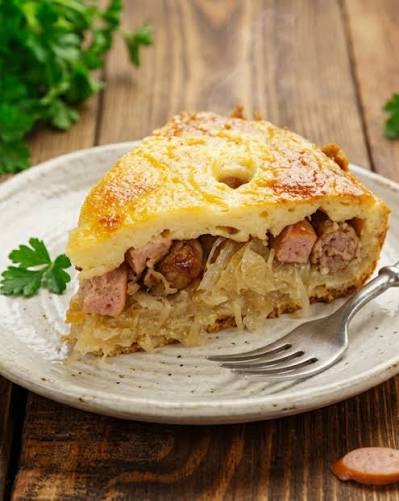 Slice of golden savory pie with sausage pieces and shredded filling on a ceramic plate