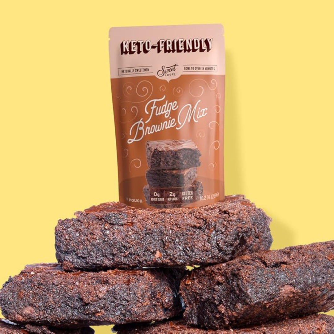 A stand-up pouch of Keto-Friendly Sweet Logic Fudge Brownie Mix stands behind a stacked pile of dark brown fudge brownies on a solid pale yellow background.