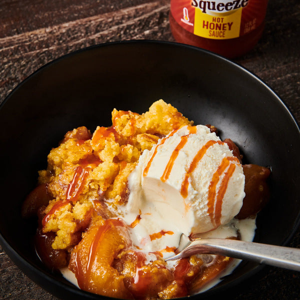 Vanilla ice cream and fruit dessert drizzled with hot honey sauce in a black bowl
