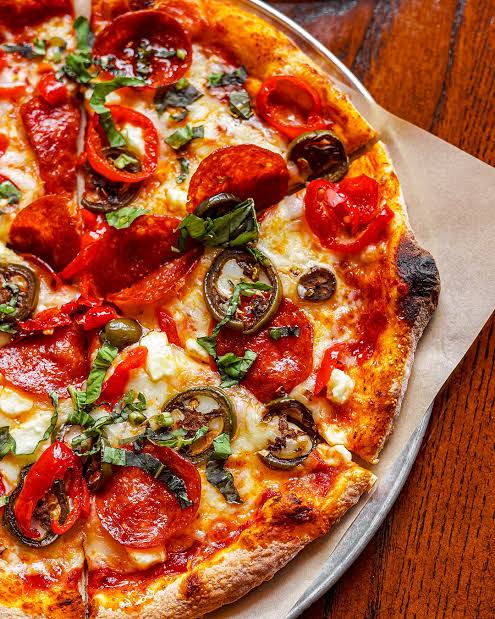 Close-up of pizza topped with pepperoni, sliced peppers, mushrooms, and herbs
