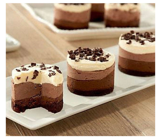 Three chocolate layer desserts topped with cream and chocolate crumbs, arranged on a white rectangular platter on a wooden table.