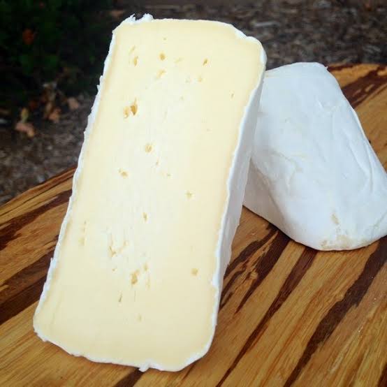 Two wedges of soft Trillium cheese with pale yellow interiors, arranged on a wooden board outdoors.