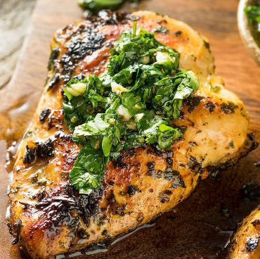 Grilled chicken breast topped with fresh green herb sauce on a wooden cutting board.