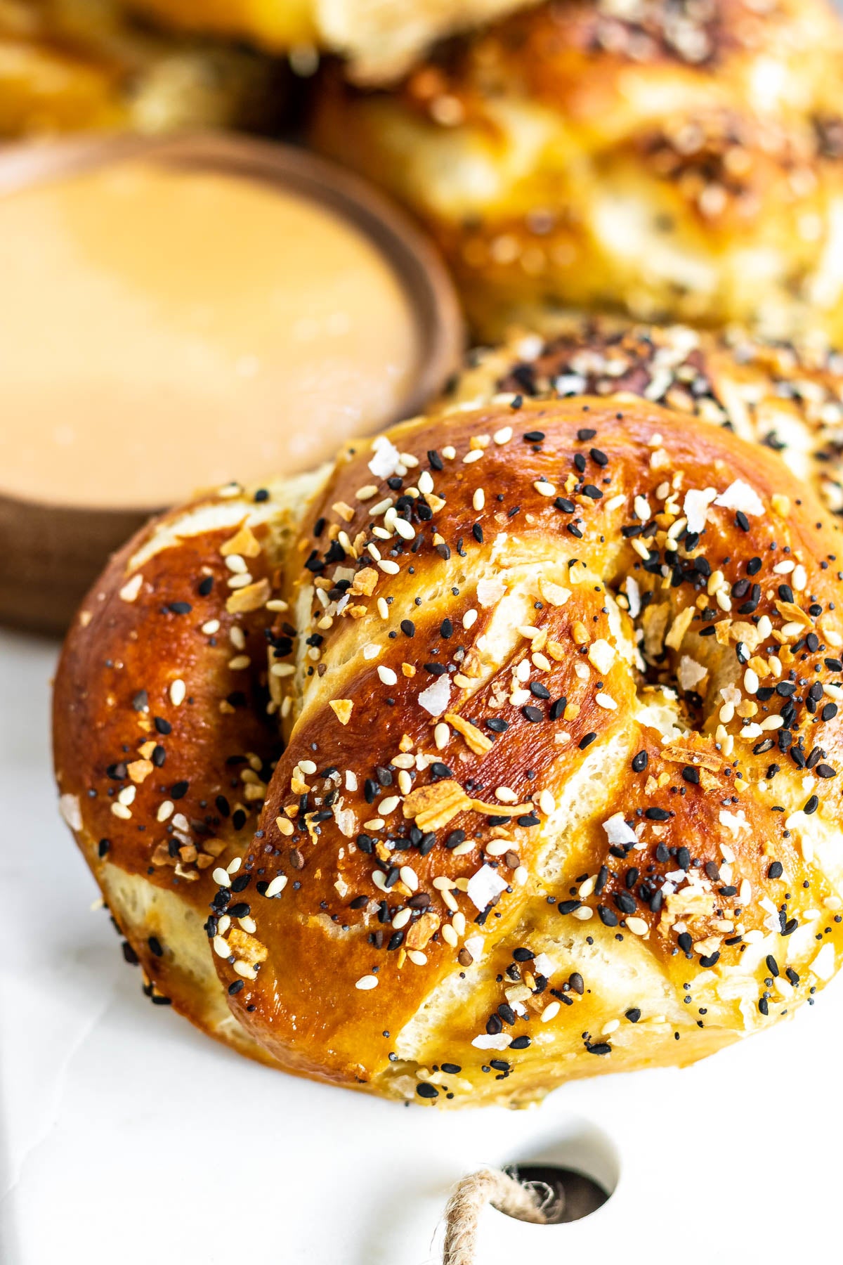Seed-topped soft pretzel beside a bowl of creamy dipping sauce.