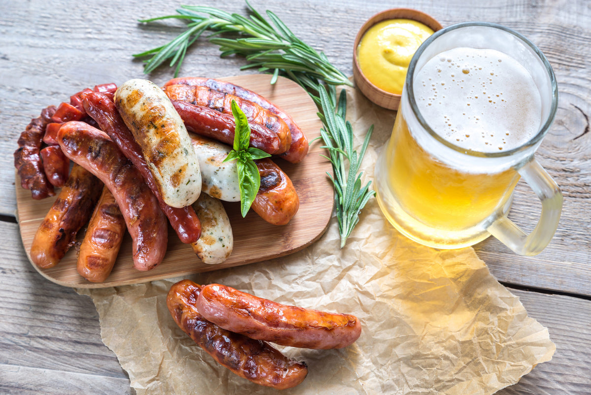Assorted grilled sausages on a wooden board with rosemary, mustard and a mug of beer.
