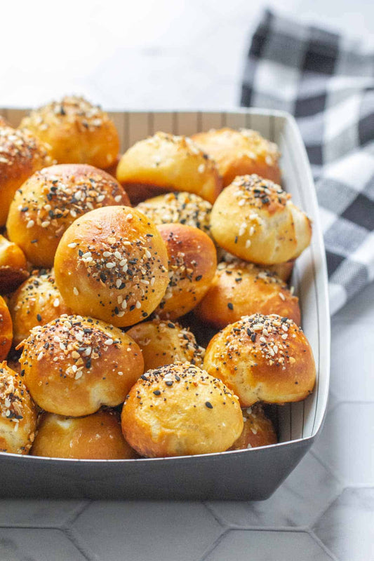 Golden pretzel bites topped with mixed seeds and seasoning in a metal tray.