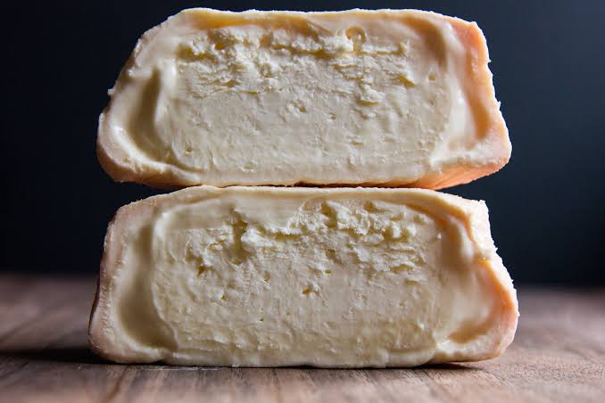 Two halves of a Foxglove cheese stacked vertically on a wooden surface against a dark background.