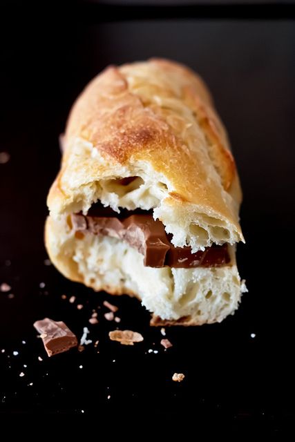 A close-up of a sliced sweet bread roll filled with chocolate and cream, set against a dark background with a few crumbs scattered nearby.