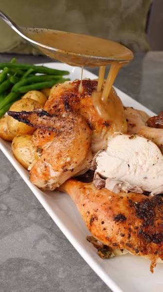 Grilled chicken served on a white rectangular platter with green beans and potatoes, with a spoon pouring brown gravy over the top.