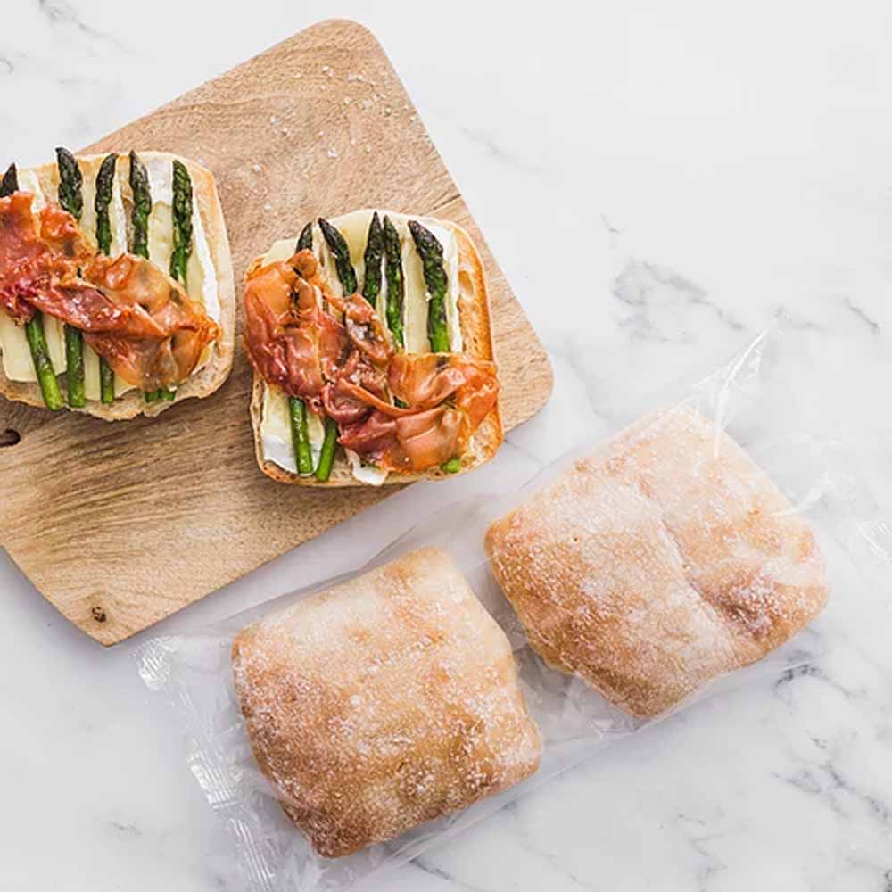 Cristal ciabatta buns served open-faced with asparagus, cheese and cured ham beside wrapped buns
