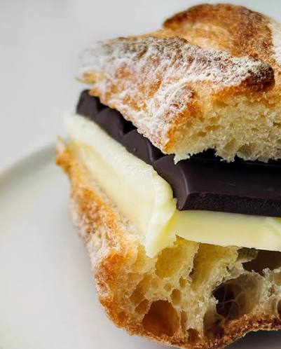 A close-up of a french baguette sandwich filled with dark chocolate and creamy butter on a white plate.