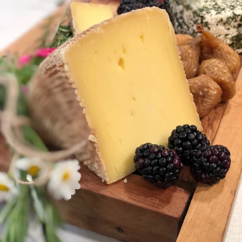 Nightshade Cheese wedge with blackberries on a wooden board with flowers in the background