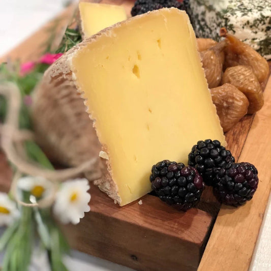 Nightshade Cheese wedge with blackberries on a wooden board with flowers in the background