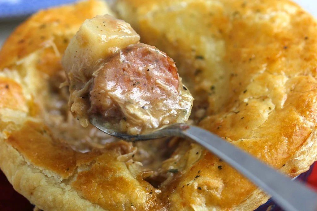 Golden pastry pie with a spoon lifting sausage and creamy filling.