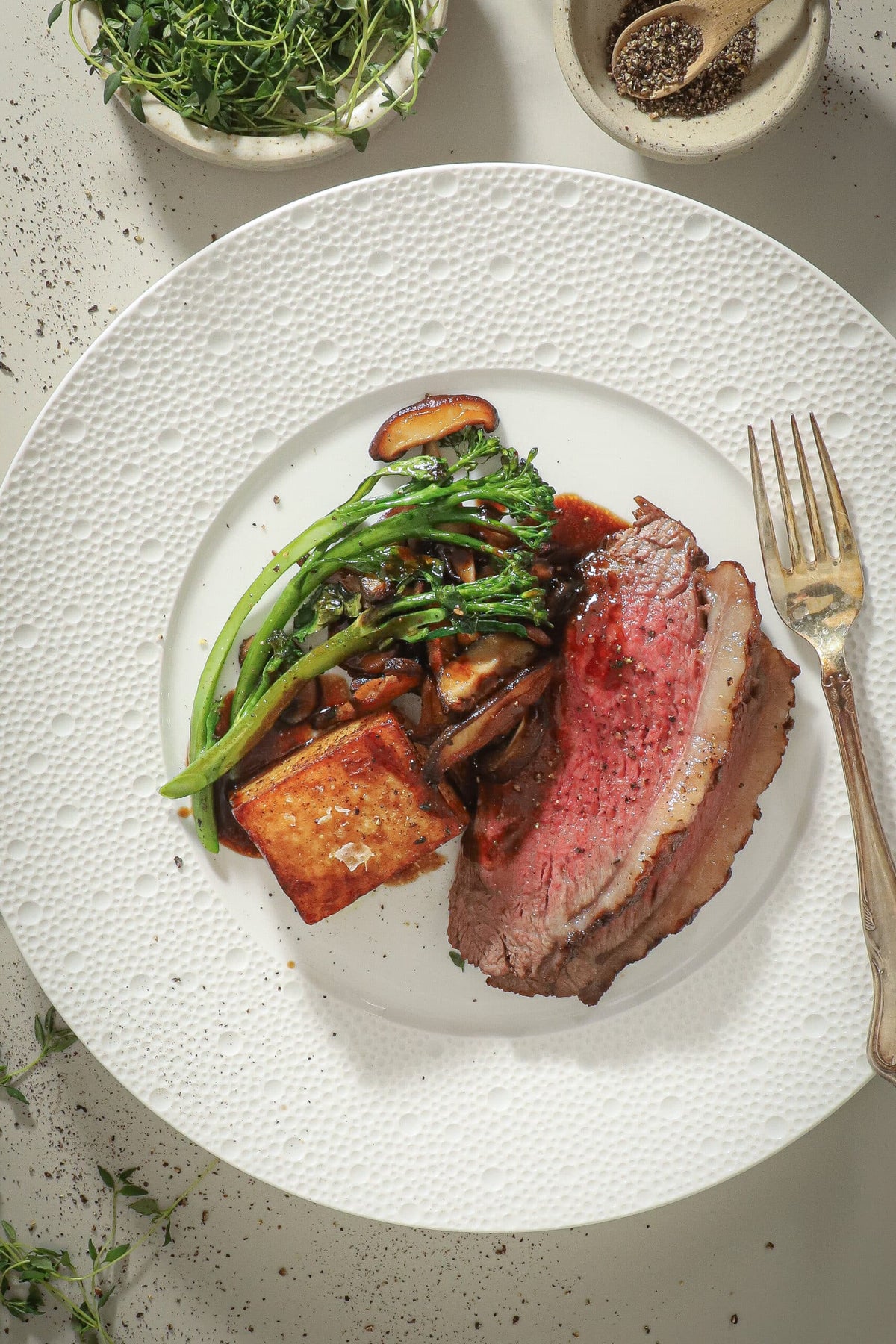 Sliced culotte beef roast served with broccolini, mushrooms, a golden potato cube, and sauce
