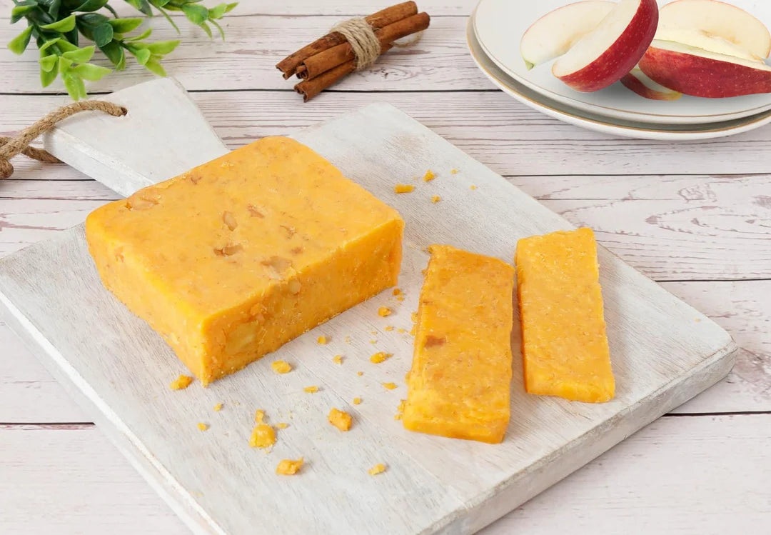 Block of Cinnamon Apple Cheddar cheese with two slices on a wooden board, apples in the background