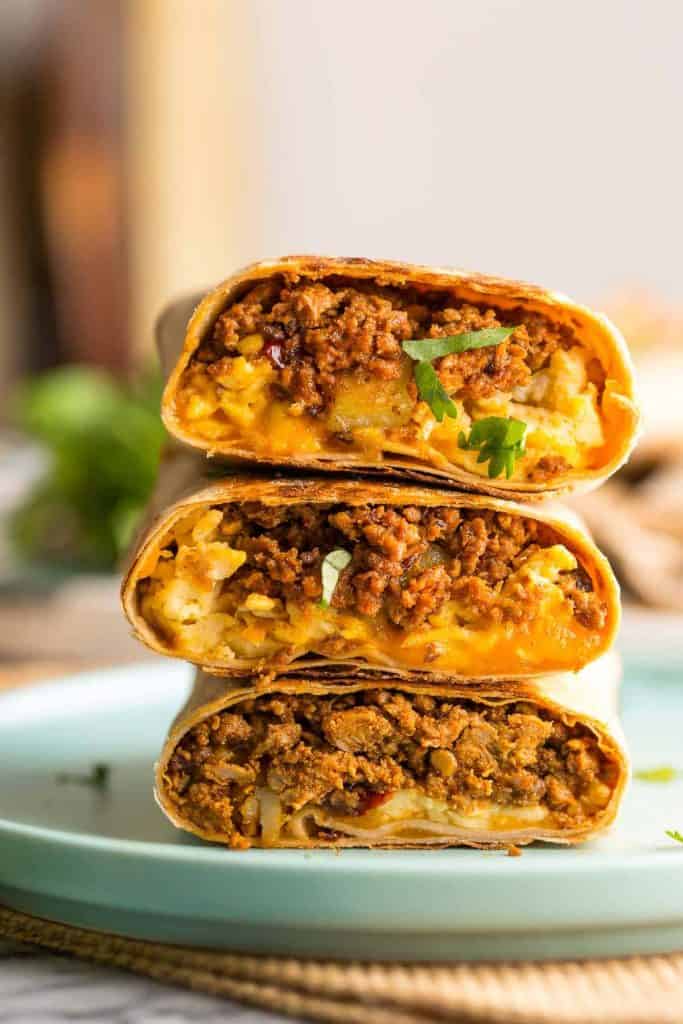 Three stacked breakfast burritos cut in half, showing a filling of ground chicken chorizo, cheese, and eggs, garnished with cilantro on a light blue plate.