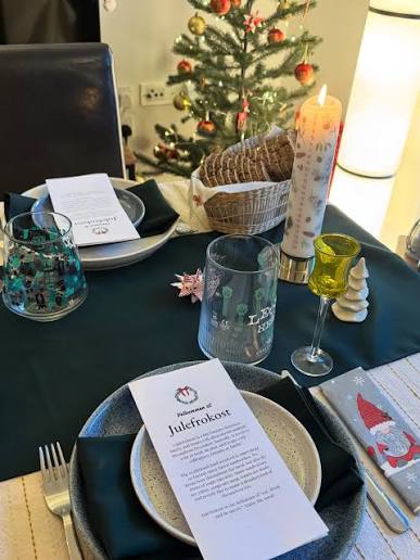 Christmas table setting with a Julefrokost menu, candles, glasses, and a bread basket.