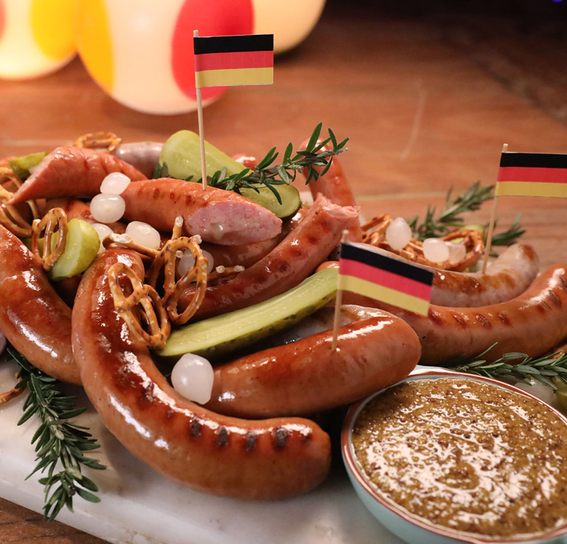 Sausage platter with pretzels, pickles, pearl onions, mustard and German flag decorations.