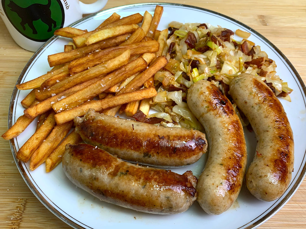 Grilled sausages served with French fries and cooked cabbage on a white plate.
