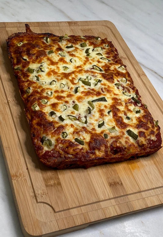 A rectangular baked casserole topped with melted cheese and sliced jalapeños, resting on a wooden cutting board over a white marble surface.