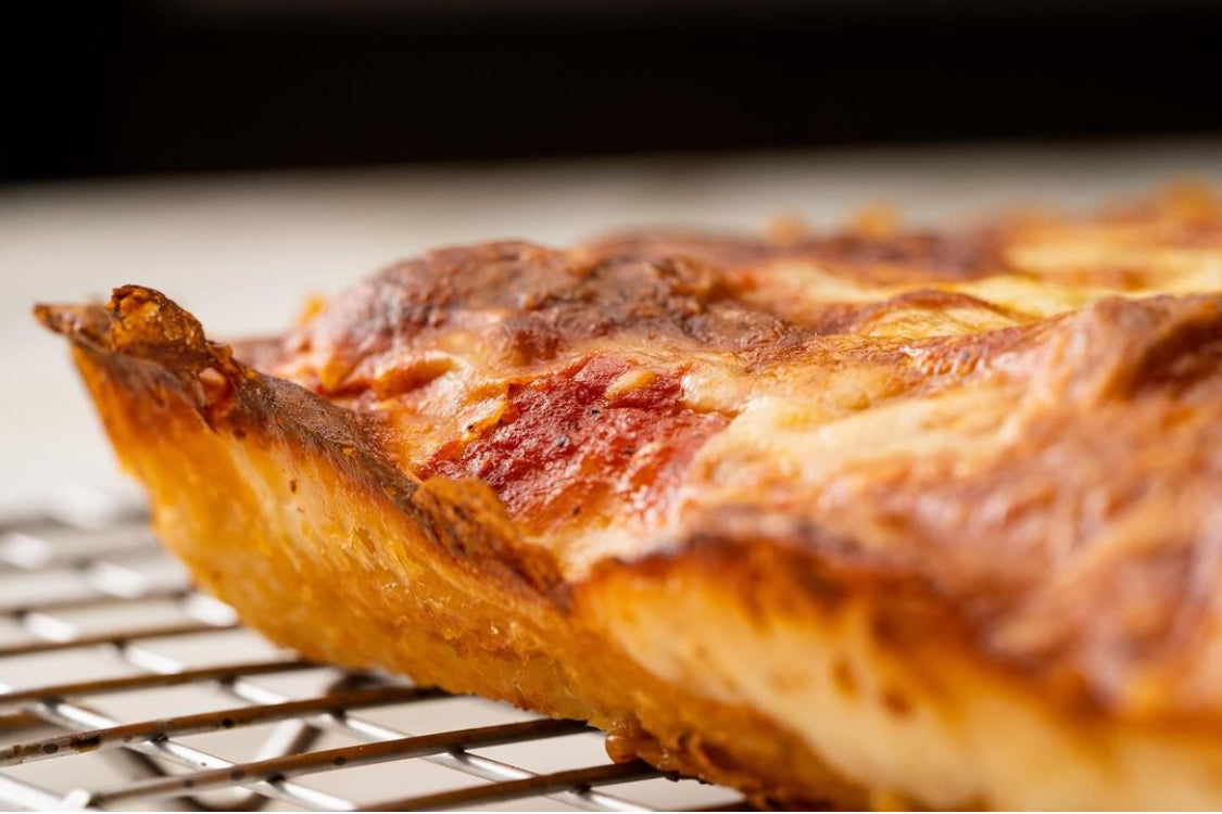 A close-up shot of a freshly baked deep-dish pizza resting on a metal cooling rack.