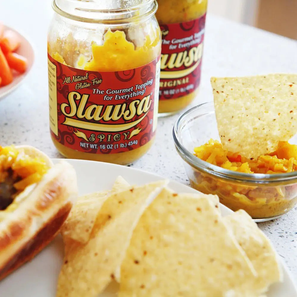 Jar of Slawsa spicy topping with tortilla chips and a bowl of the topping on a table.