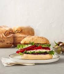 Burger with lettuce and tomato on a Cristal ciabatta bun, with packaged buns in the background
