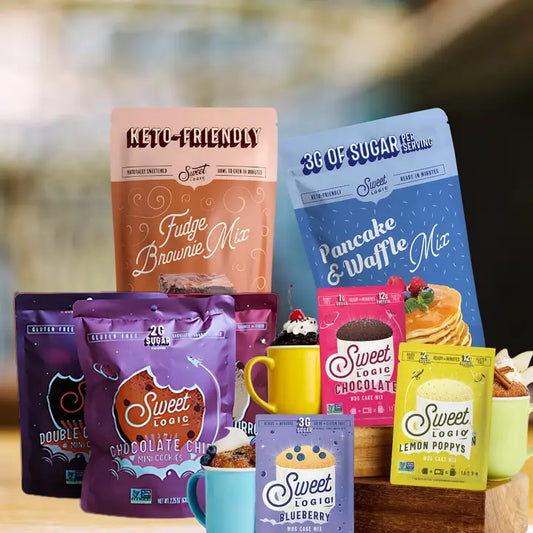 A collection of Sweet Logic keto-friendly coffee and dessert mixes displayed on a wooden shelf with colorful mugs. The products include Fudge Brownie Mix, Pancake & Waffle Mix, Chocolate Chip Cookie Mix, Blueberry Pancake Mix, Lemon Poppys Mix, and Double Chocolate Cookie Mix, shown in various vibrant packaging colors like blue, purple, pink, and yellow.