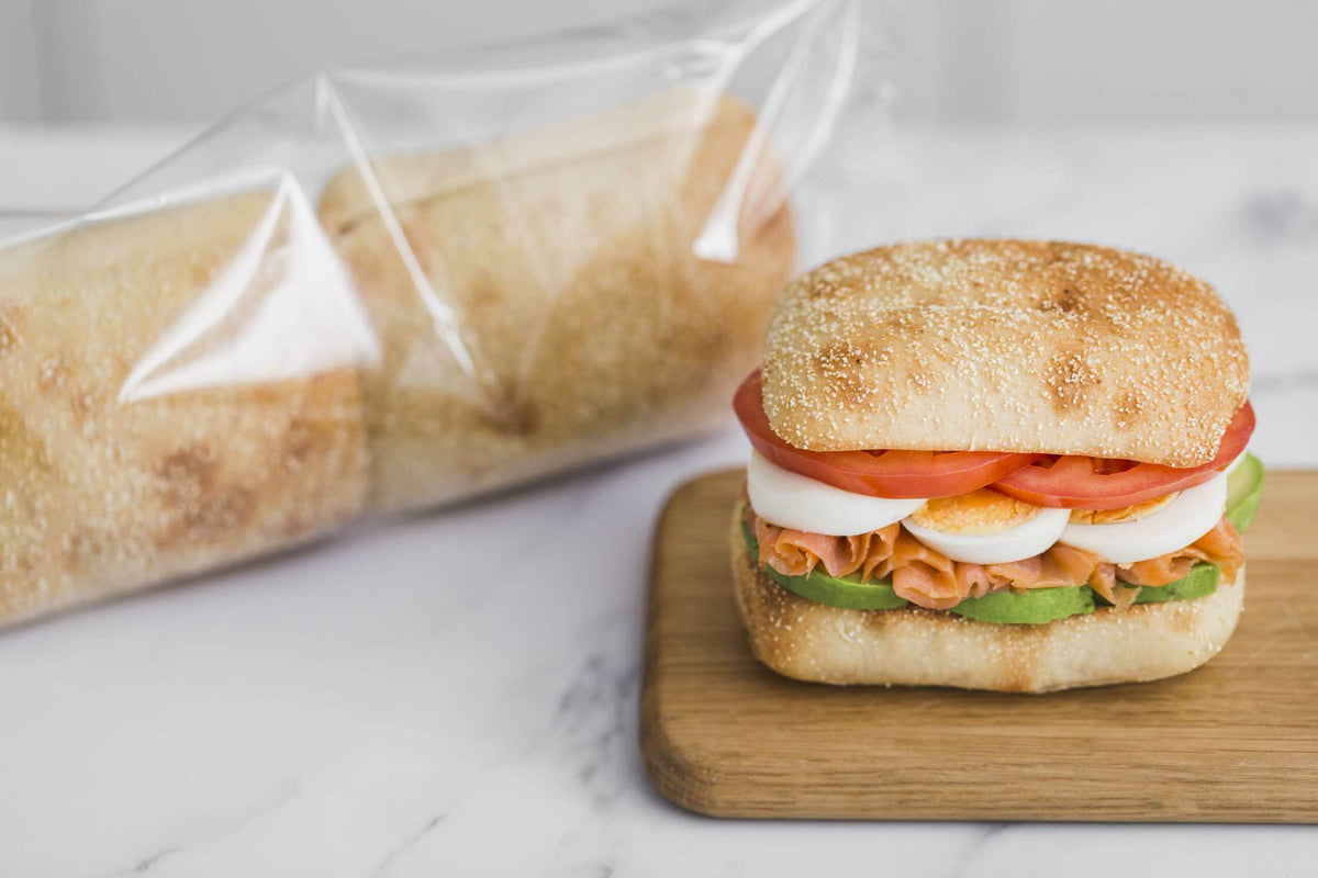Cristal ciabatta bun sandwich with sliced egg, tomato, avocado and salmon on a wooden board

