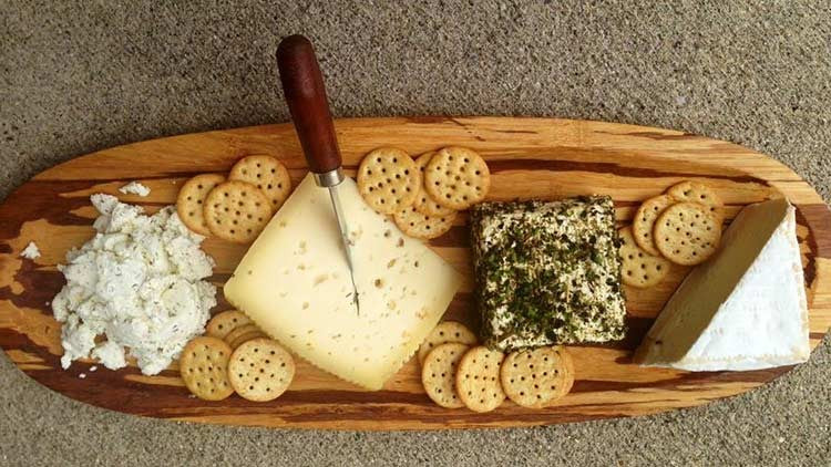 An overhead view of a wooden charcuterie board with crackers, cheese, and a knife on a textured gray surface.