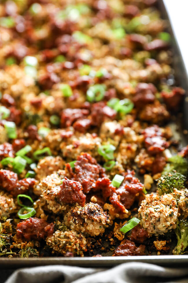 A close-up shot of a roasted vegetable and ground chicken chorizo mixture on a baking sheet, featuring broccoli, red sauce, and chopped green onions.