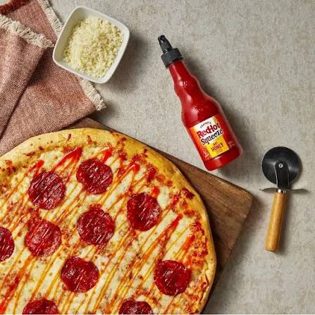 Pepperoni pizza drizzled with sauce beside a Frank’s RedHot Squeeze Hot Honey Sauce bottle
