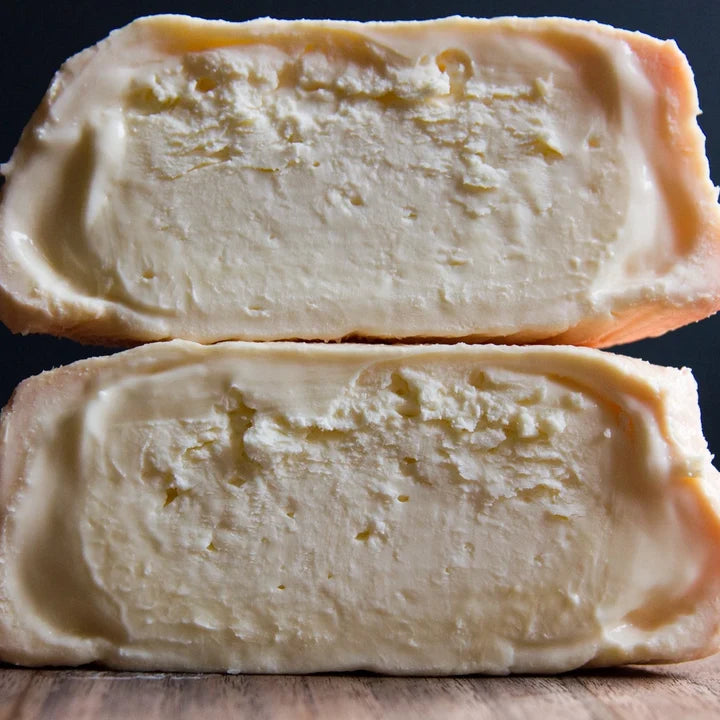 Two halves of a Foxglove cheese wheel stacked vertically, showing the textured rind and creamy interior against a dark background.
