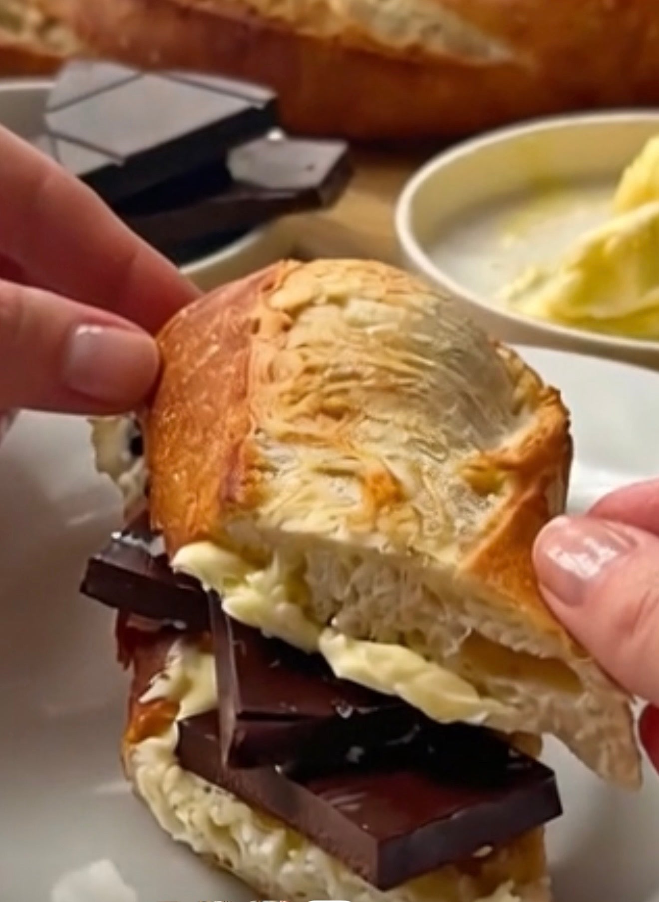 A close-up of a hand holding a baguette sandwich filled with dark chocolate and buerre butter, showing more chocolate and butter.