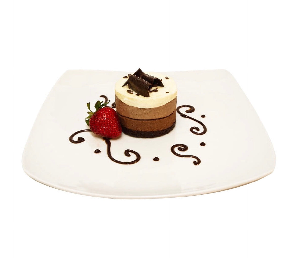 A small layered chocolate dessert cake with a cream-colored top and chocolate shavings, served on a white square plate with a strawberry and chocolate drizzle.