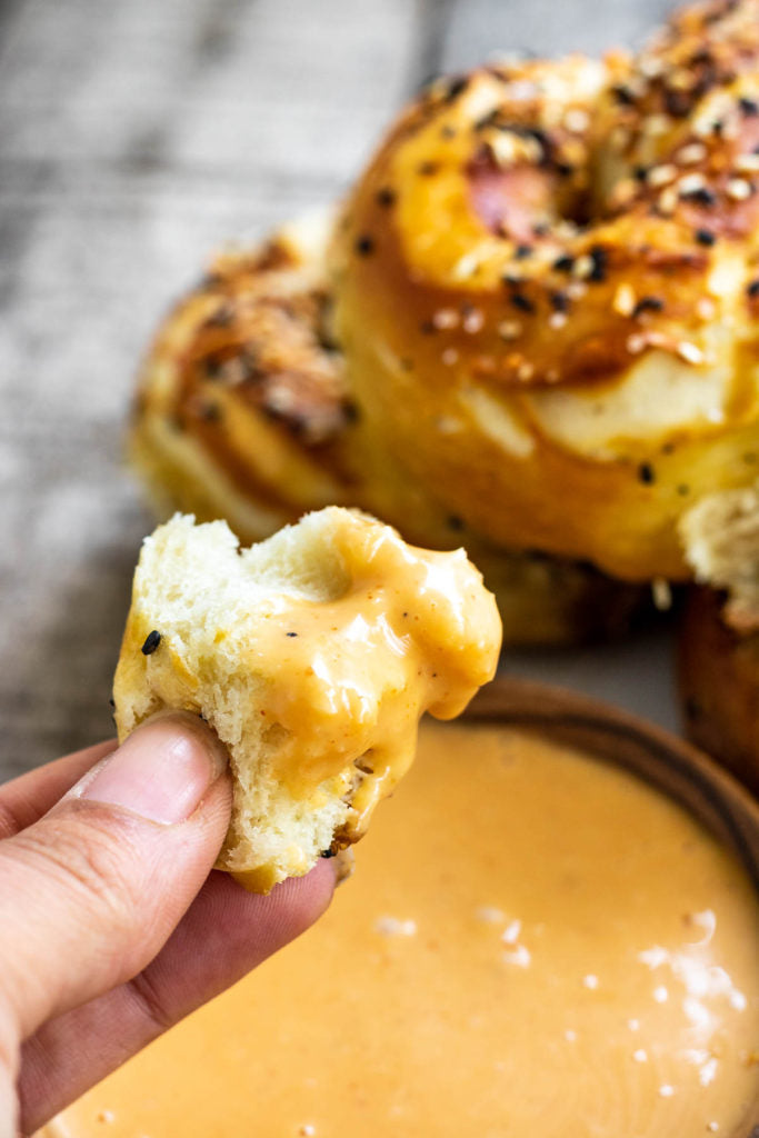 “Hand holding a torn pretzel piece dipped in creamy orange sauce.