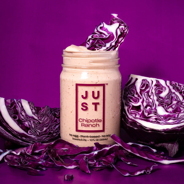 A jar of Chipotle Ranch creamy sauce on a vibrant purple background, styled with fresh red cabbage halves and shreds around it.