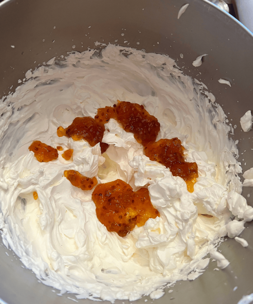 Whipped white cream metal mixing bowl with dollops of cloudberry jam on top.