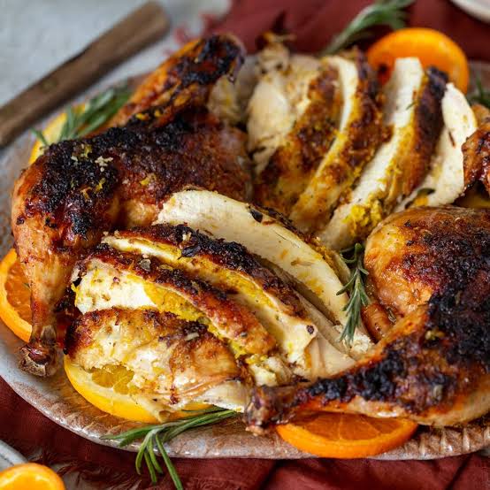 Sliced roasted chicken with crispy browned skin, served on a plate with orange slices and rosemary garnish.