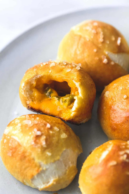 Salted pretzel bites on a plate, with one opened to show yellow filling and green pieces.